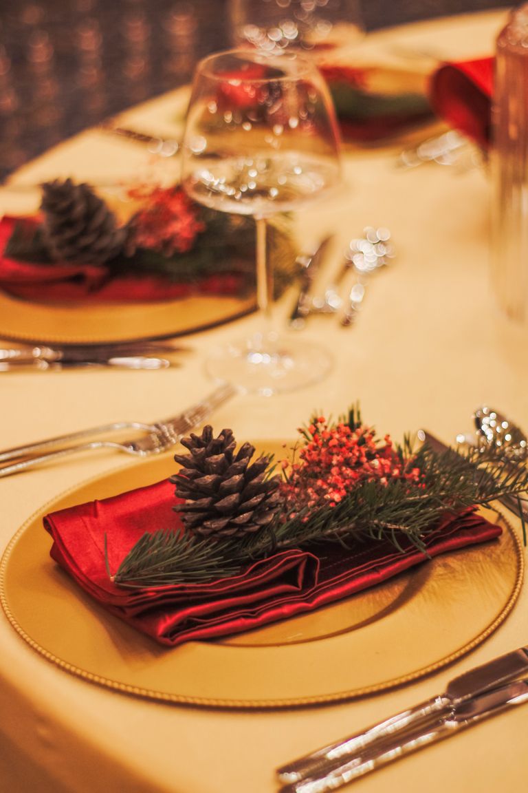 Festive Christmas table setting with pine cones, red napkins, and elegant glassware.